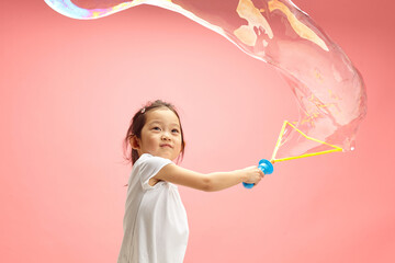 Funny Little Asian Girl Making Big Soap Bubbles on Pink Isolated