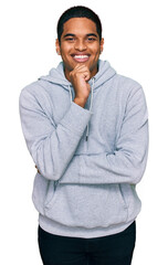 Young handsome hispanic man wearing casual sweatshirt looking confident at the camera with smile with crossed arms and hand raised on chin. thinking positive.