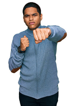 Young handsome hispanic man wearing casual sweatshirt punching fist to fight, aggressive and angry attack, threat and violence