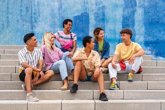 Multi ethnic group of young people sitting on steps in front of wall
