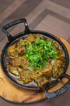 Close-up of the traditional Georgian dish ostri sprinkled with herbs in a cast-iron pan on a wooden board on the table. Vertical photo