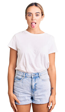 Young beautiful blonde woman wearing casual white tshirt sticking tongue out happy with funny expression. emotion concept.
