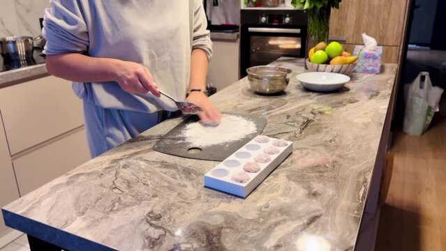 A woman is making cookies on a marble countertop. She is using a spatula to mix the dough