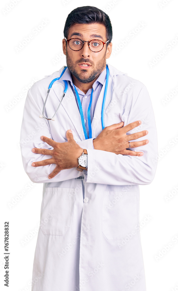Wall mural Young hispanic man wearing doctor uniform and stethoscope shaking and freezing for winter cold with sad and shock expression on face - Wall murals