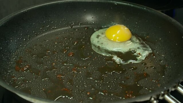 Sunny side up raw egg is cracked into hot non-stick skillet on stove
