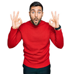 Young hispanic man wearing casual clothes looking surprised and shocked doing ok approval symbol with fingers. crazy expression