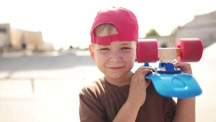 child boy with a skateboard. boy in a red cap with a skateboard on the playground portrait. skateboarder child close-up outdoors sun glare lifestyle. kid skateboarder looking at the camera - 767832065