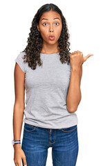 Young african american girl wearing casual clothes surprised pointing with hand finger to the side,...