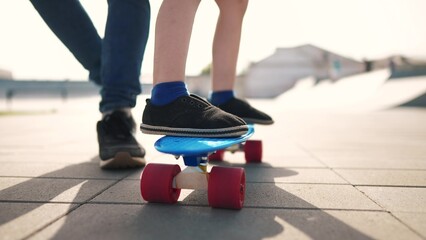 learn to skateboard. dad teaches daughter to ride a skateboard outdoors at the playground. father and daughter play training concept. parent teaching child lifestyle daughter to skateboard - 767832444