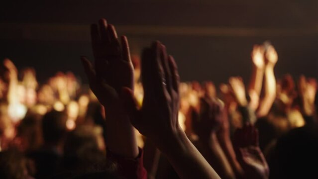 Cheering hands at a concert in front of a large stage in the spotlight close-up