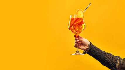 Hand hold delicious Aperol Spritz cocktail garnished with slice of orange against orange background...