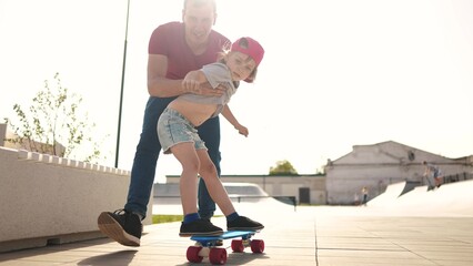 learn to skateboard. dad teaches daughter to ride a skateboard outdoors at the playground. father and daughter play training concept. lifestyle parent teaching child daughter to skateboard - 767833807