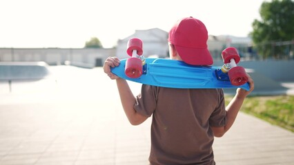 child walk with a skateboard. boy in a red cap with a skateboard on the playground portrait. skateboarder child walk outdoors sun glare. kid skateboarder lifestyle to the skatepark - 767834894