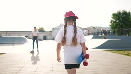 child walk with a skateboard. girl in a red cap with a skateboard on the playground portrait. skateboarder child walk outdoors sun glare lifestyle. kid skateboarder lifestyle to the skatepark - 767835021