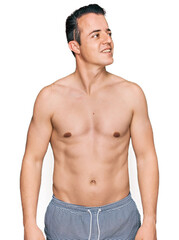 Fototapeta premium Handsome young man wearing swimwear shirtless looking away to side with smile on face, natural expression. laughing confident.