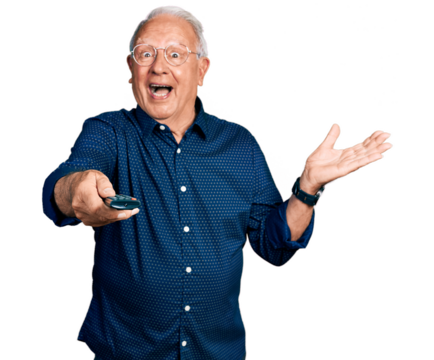 Senior man with grey hair holding television remote control celebrating achievement with happy smile and winner expression with raised hand