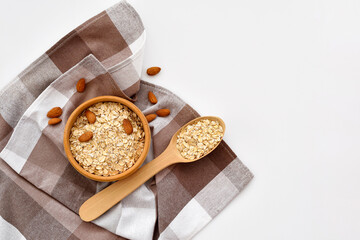 Oatmeal in a wooden bowl with almonds and scattered oat flakes and with spoon on white background. View from above. Place for text - 767840290