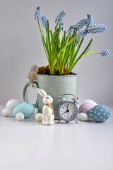 Easter composition with white rabbit, eggs, clock and spring flowers. Happy Easter holiday concept. Front view.