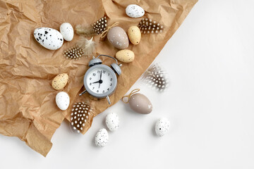 Easter eggs with clock and feathers on a brown kraft paper background on a white table. Top view. For easter greeting cards with copy space.