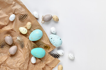 Easter eggs and feathers on a brown kraft paper background on a white table. Top view. For easter greeting cards with copy space.