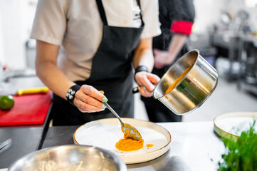 Professional chef artistically plating vibrant orange sauce in a kitchen, showcasing culinary...