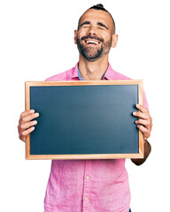 Hispanic man with ponytail holding blackboard smiling and laughing hard out loud because funny...