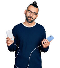 Hispanic man with ponytail holding portable battery charger relaxed with serious expression on...