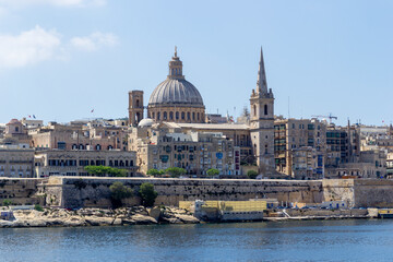 Fototapeta na wymiar Valletta, Malta - June 9th 2016: The fortified capital city Valletta with the dome of Basilica of Our Lady of Mount Carmel and the tower of Saint Paul's Pro-Cathedral overlooking Marsamxett Harbour.