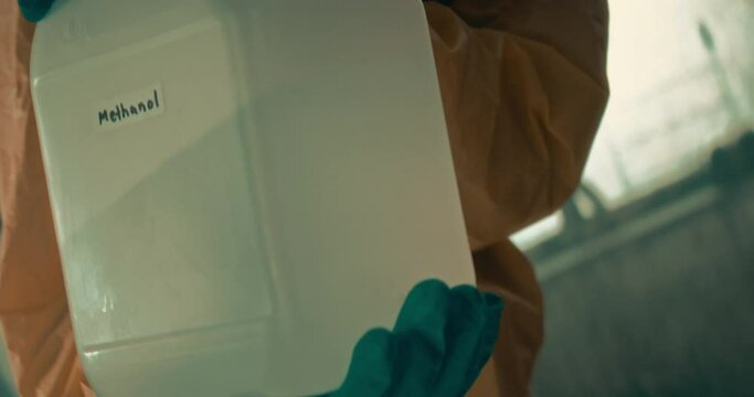 The video depicts a man in a chemical safety suit opening a bottle of methanol and precisely pouring the chemical into lab equipment, highlighting meticulous safety measures during the experiment.