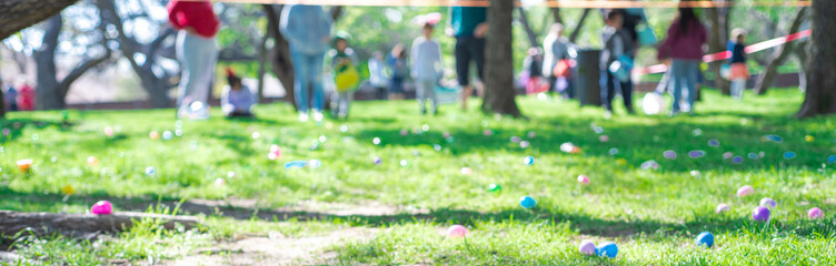 Panorama abundant of colorful Easter eggs on green grass field with blurry diverse people kids...
