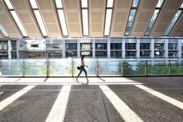 午後の光差し込む品川インターシティーデッキを歩く女性 © masyok