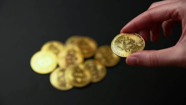 Hand showing a bitcoin and a pile of bitcoins out of focus on a black background. Bullish BTC, cryptocurrency, 2p2 exchange and blockchain concept