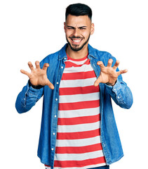 Young hispanic man with beard wearing casual denim jacket smiling funny doing claw gesture as cat,...
