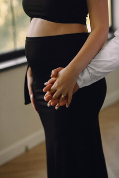 Close up photo of pregnant belly. Pregnant woman in black dress and her husband holding their hands while posing in the studio. Love concept. Family concept