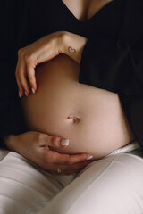 Pregnant woman in black jacket and white pants holding her belly in the studio. Close up photo of...