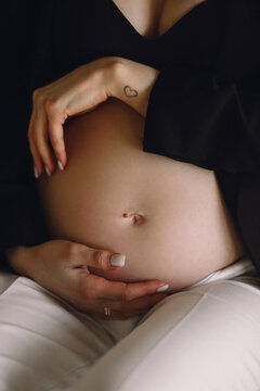 Pregnant woman in black jacket and white pants holding her belly in the studio. Close up photo of pregnant belly. Love concept. Birthmark on a stomach.
