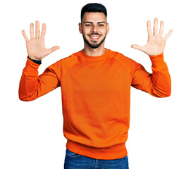 Naklejka premium Young hispanic man with beard wearing casual orange sweater showing and pointing up with fingers number ten while smiling confident and happy.