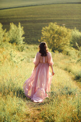 Rear view of attractive brunette woman in pink flying dress fluttering on wind. Young female walking on nature at summertime