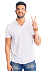 Young handsome hispanic man wearing casual clothes showing and pointing up with fingers number two while smiling confident and happy.