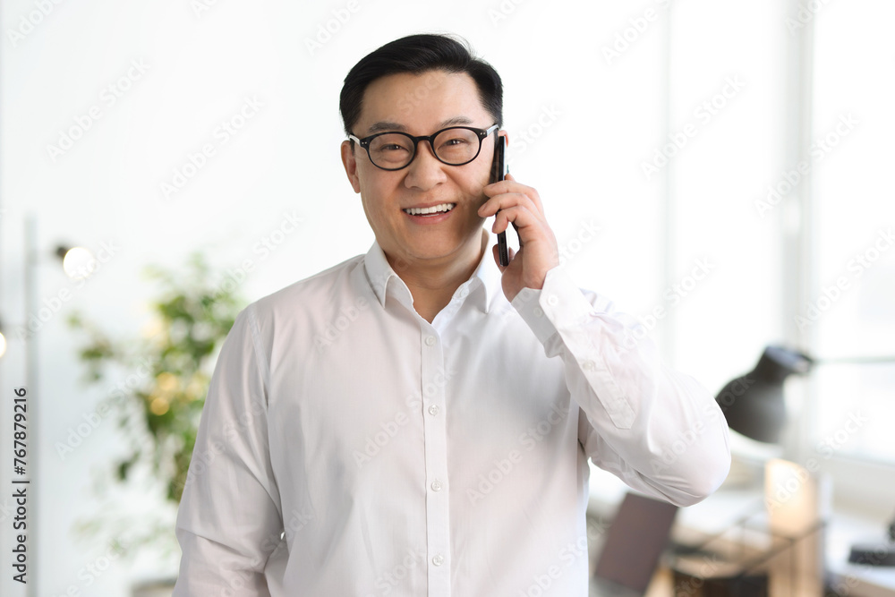 Wall mural Portrait of smiling businessman talking by smartphone in office