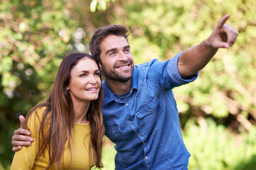 Happy couple, women and man pointing in nature or park for bonding, dating and relationship with smile. People, love and romantic in backyard or outdoor with joy, excited and commitment in marriage