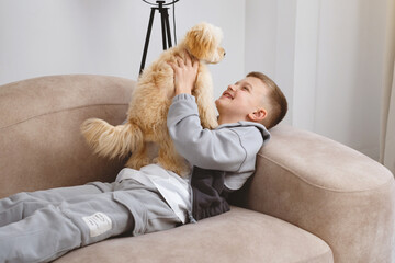 Young boy is relaxing on a couch, affectionately holding a maltipoo dog in his arms