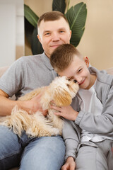 Man and boy sitting on couch with a dog, relaxing indoors with family.