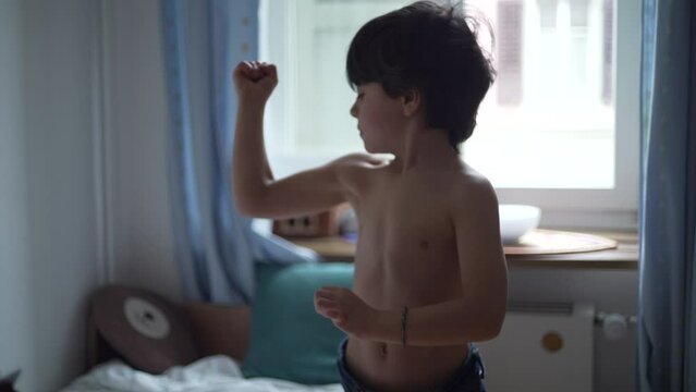 Adorable little boy showing his muscles, happy 5 year old male caucasian child flexing arms in bedroom
