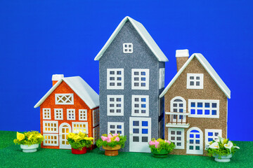 Three toy houses of different heights with flowers nearby on a blue background
