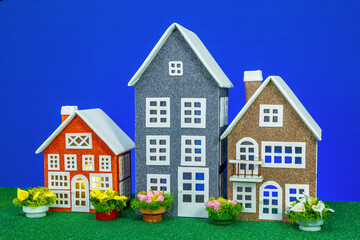 Three toy houses of different heights and different colors with flowers nearby on a blue background