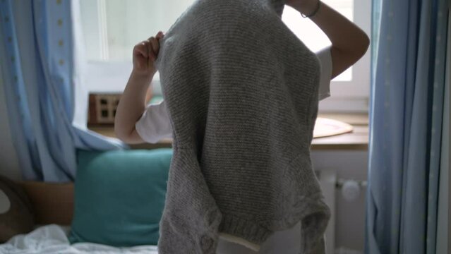 Little boy putting pullover standing in bedroom. 5 year old caucasian male kid dressing by himself clothing warm clothes during cold season
