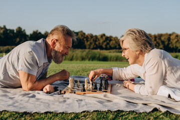 Retired man and woman competing in game of chess outside - 767884810