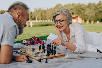 Couple lying on rug and playing chess in public park - 767884817