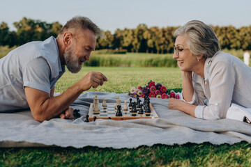 Grey-haired couple playing chess on fresh air
